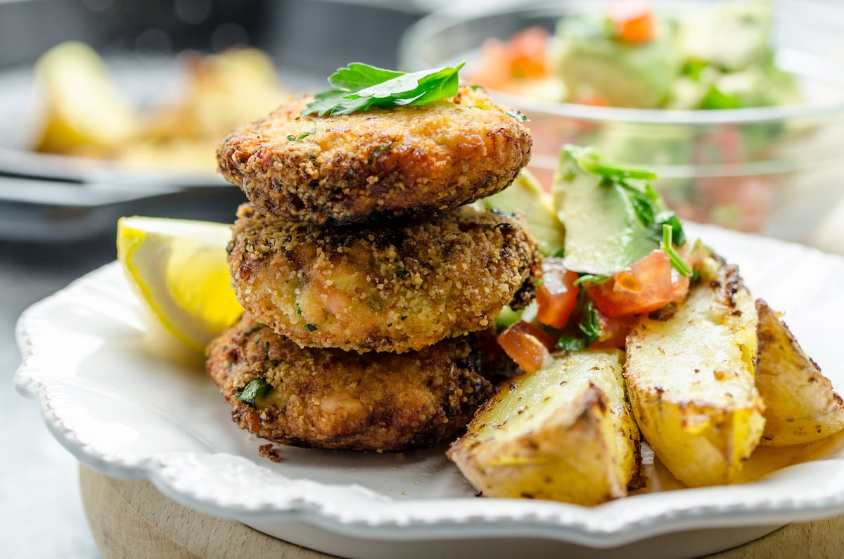Close-up of salmon croquettes on a plate with tomato avocado salsa and skillet fries