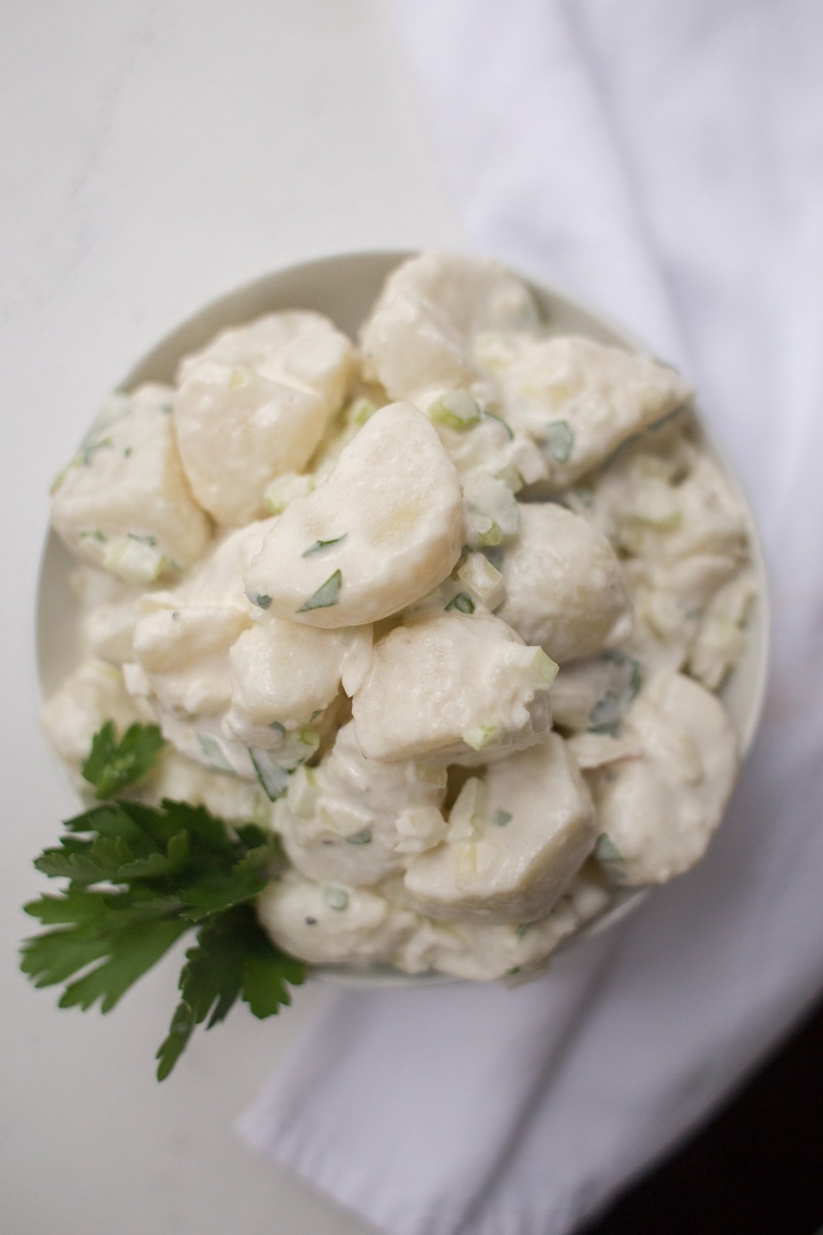 top down view of eggless potato salad in a white bowl
