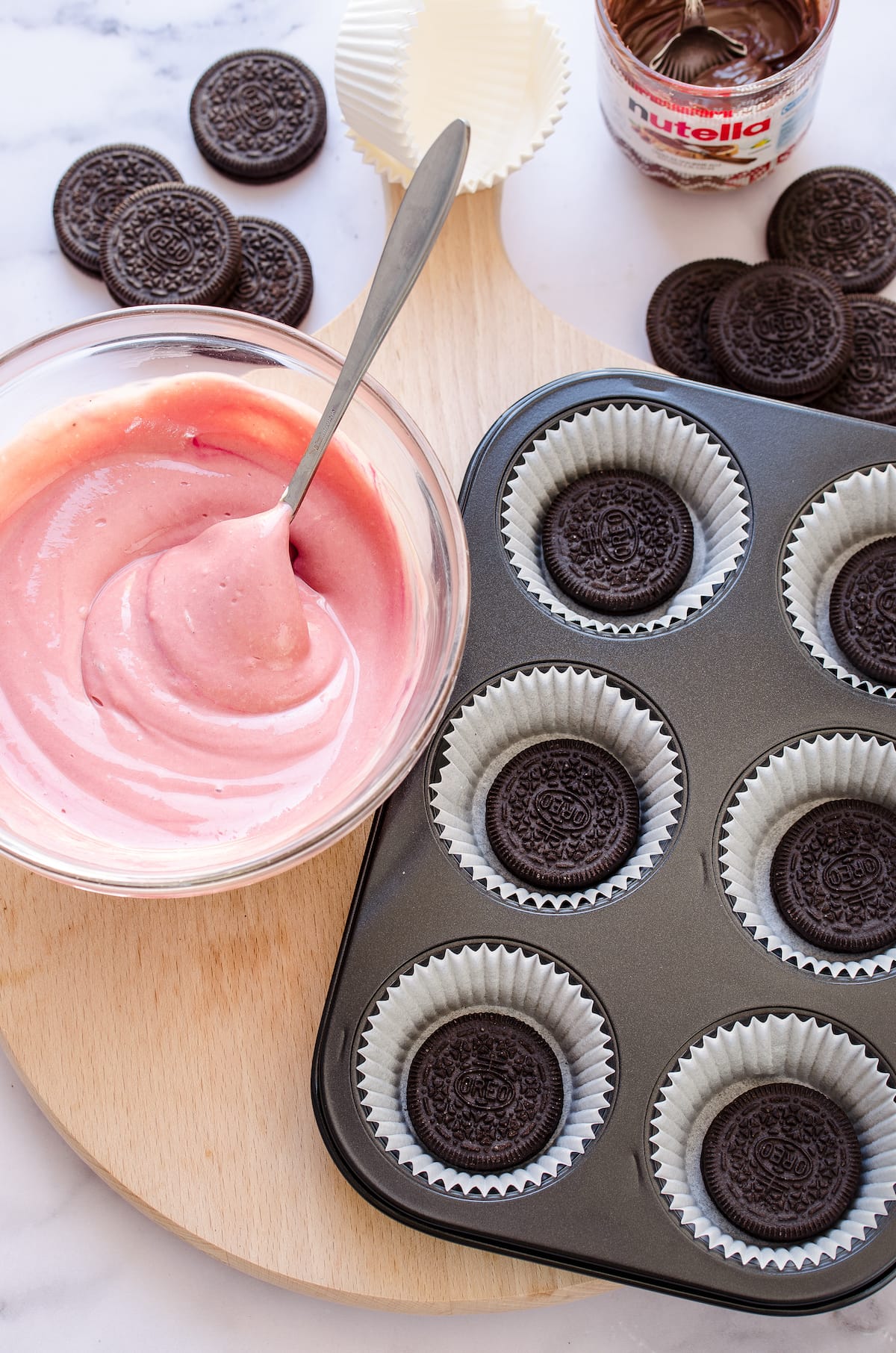 A bowl of red velvet cheesecake batter next to a muffin pan with Oreos in each cupcake liner