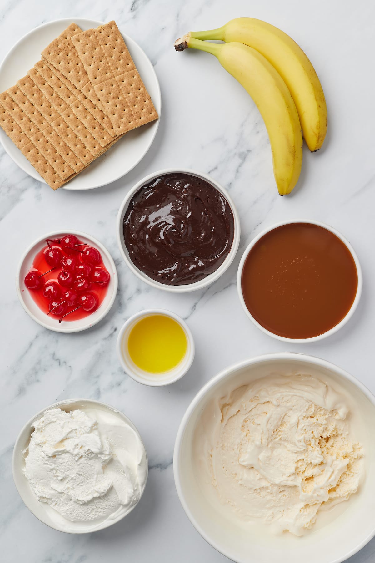 From top left: Graham crackers, bananas, maraschino cherries, hot fudge sauce, caramel suace, butter, whipped cream, vanilla ice cream.