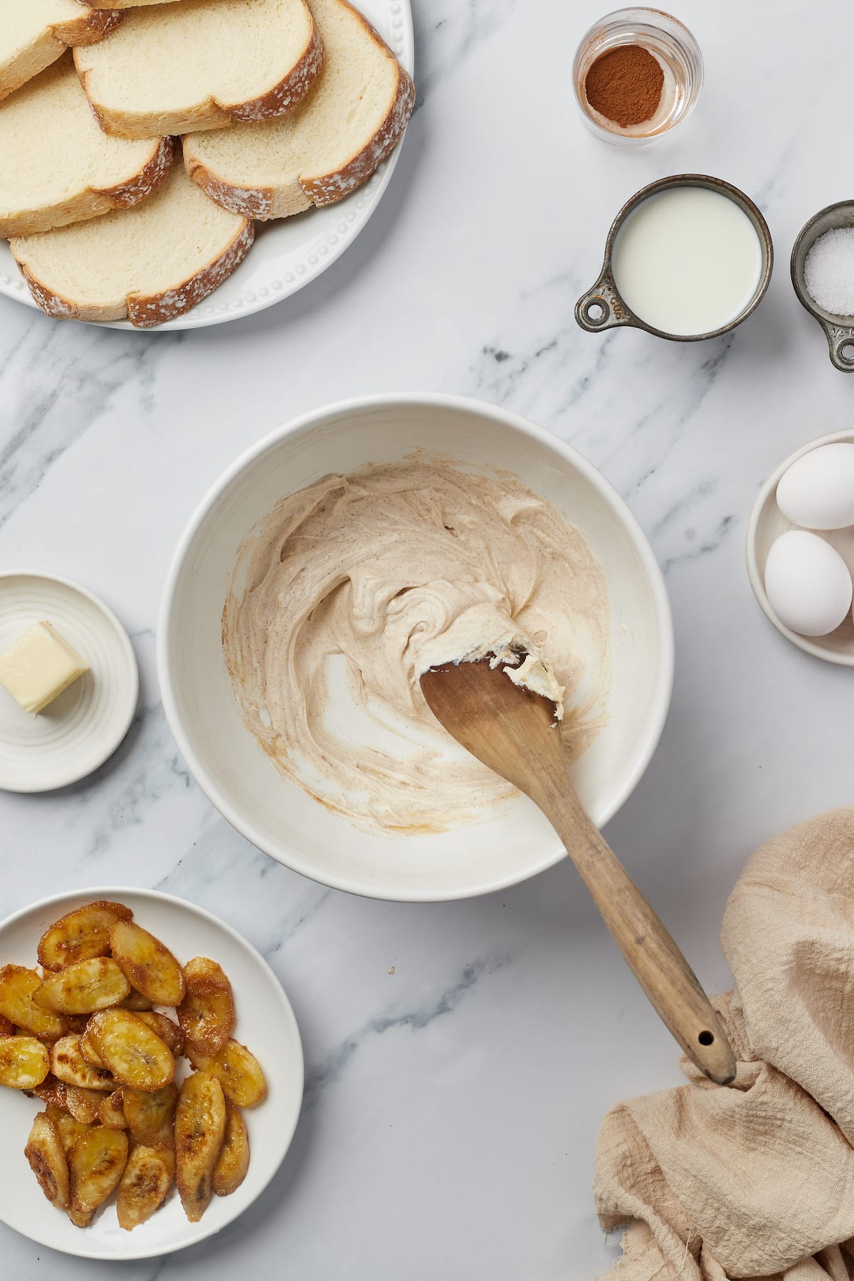 A white mixing bowl with cream cheese filling and a wooden spoon.