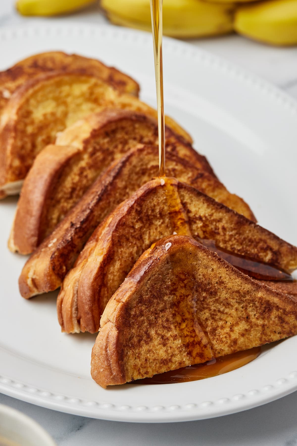 Maple syrup being poured over French toast on a serving platter.