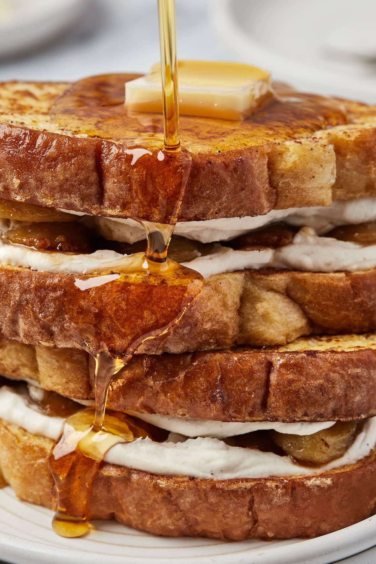Maple syrup running down the sides of sandwiched French toast with cream cheese filling.
