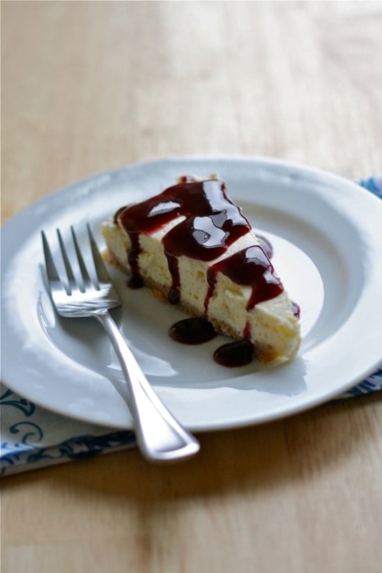 new york style blackberry cheesecake slice on a white plate with a fork
