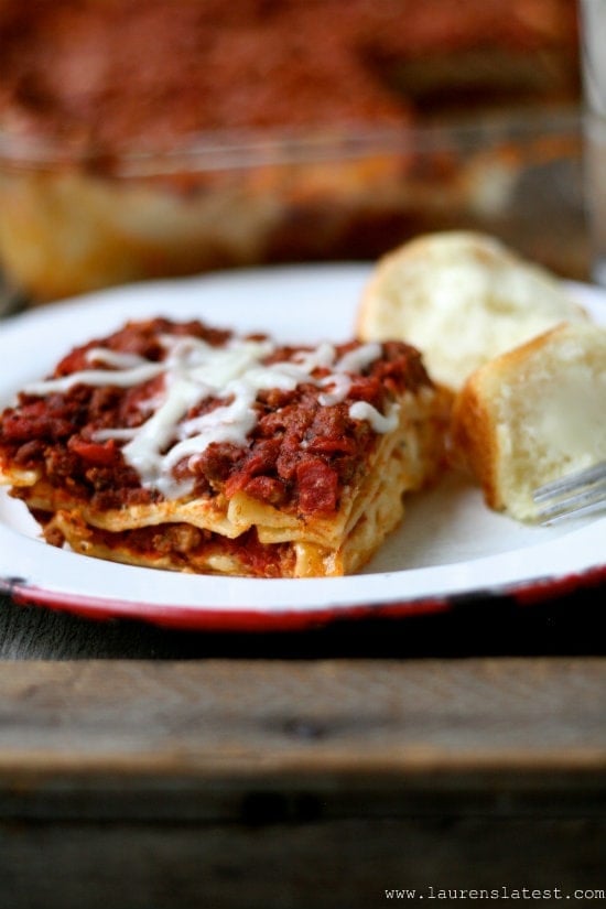 Slice of lasagna on a white plate with rolls