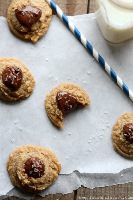 Top down view of Peanut Butter Thumbprint Cookies on parchment paper. One cookie has a bite taken out of it.