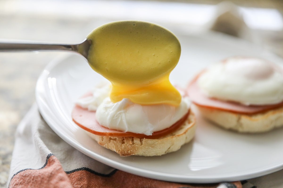 pouring hollandaise sauce over poached egg