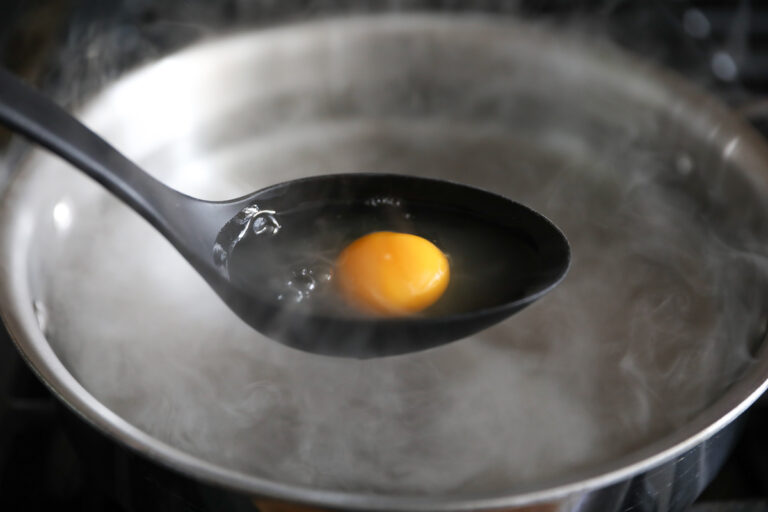 raw egg in large spoon hovering over simmering water