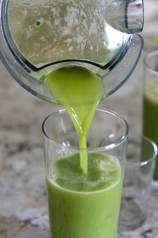 pouring green juice into a glass cup