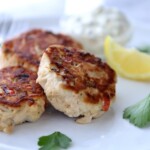 Three tuna patties on a white plate with lemon wedges.