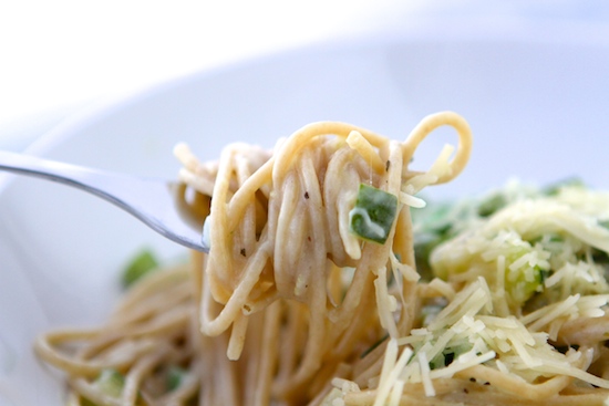 A fork is holding a bowl of lemon basil pasta with greens and parmesan cheese.