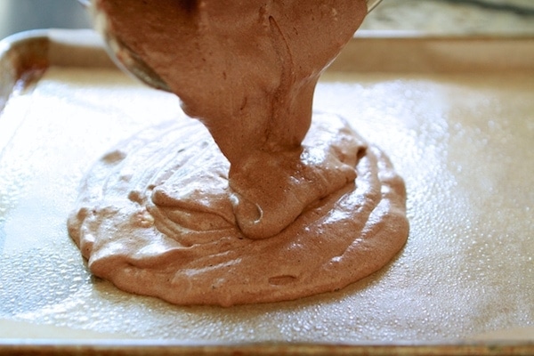 pouring chocolate swiss roll cake batter into a greased baking sheet