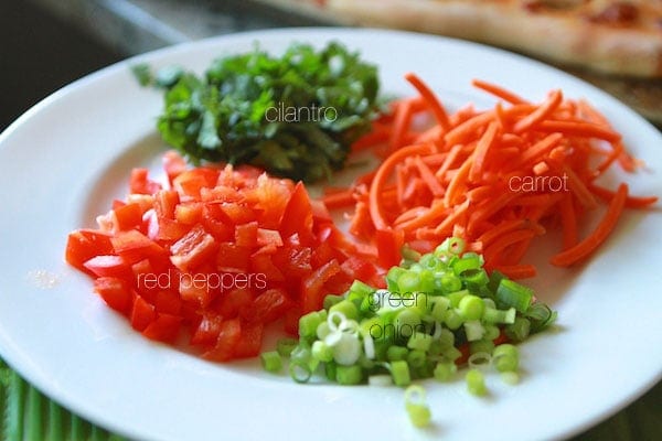 chopped cilantro, red peppers, green onion and carrot on a plate