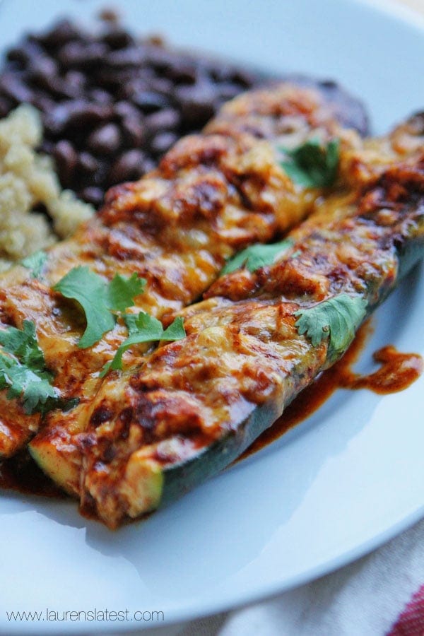 side view of Zucchini Enchiladas on a white plate next to beans and rice