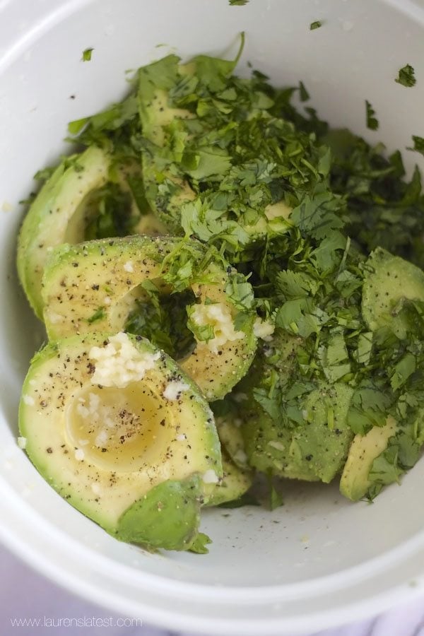 Super Bowl guacamole recipe with avocados in a white bowl topped with cilantro and parsley.