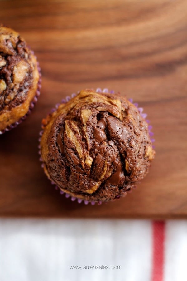 Two banana almond butter muffins on a wooden cutting board.