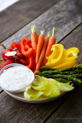 A plate of vegetables and Ranch Dressing on a wooden table.