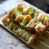 Chicken skewers are served on a white plate with lime slices.