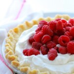A pie with whipped cream and raspberries on top, perfect for dessert.