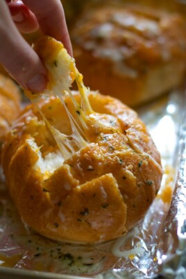 A person is dipping a piece of bread into melted cheese, reminiscent of enjoying  pull apart garlic bread.