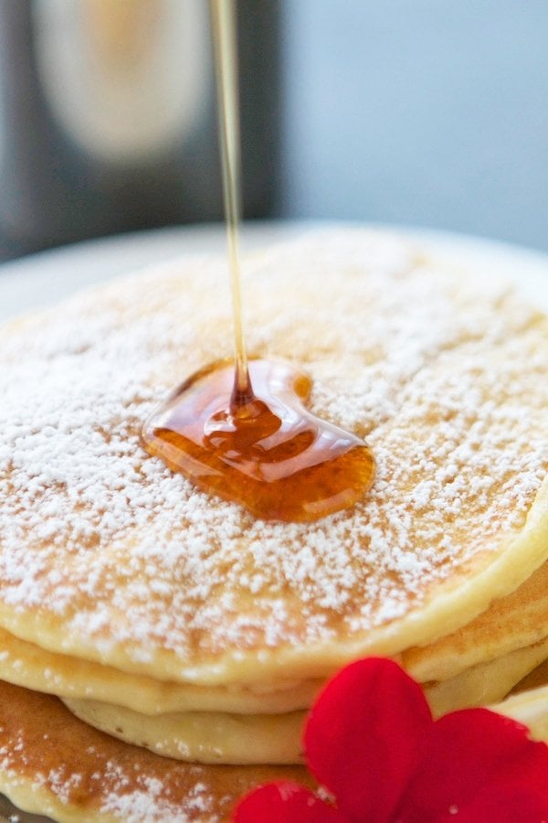 pouring syrup over lemon ricotta pancakes dusted in powdered sugar