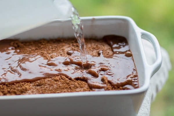 pouring water over chocolate cobbler topping in a baking dish