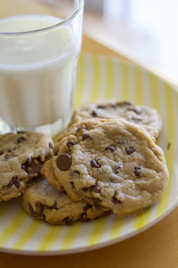 brown butter chocolate chip cookies on a white and yellow plate next to a glass of milk