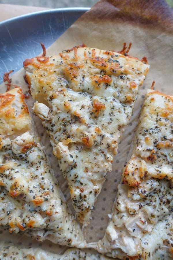 sliced chicken alfredo pizza on parchment paper