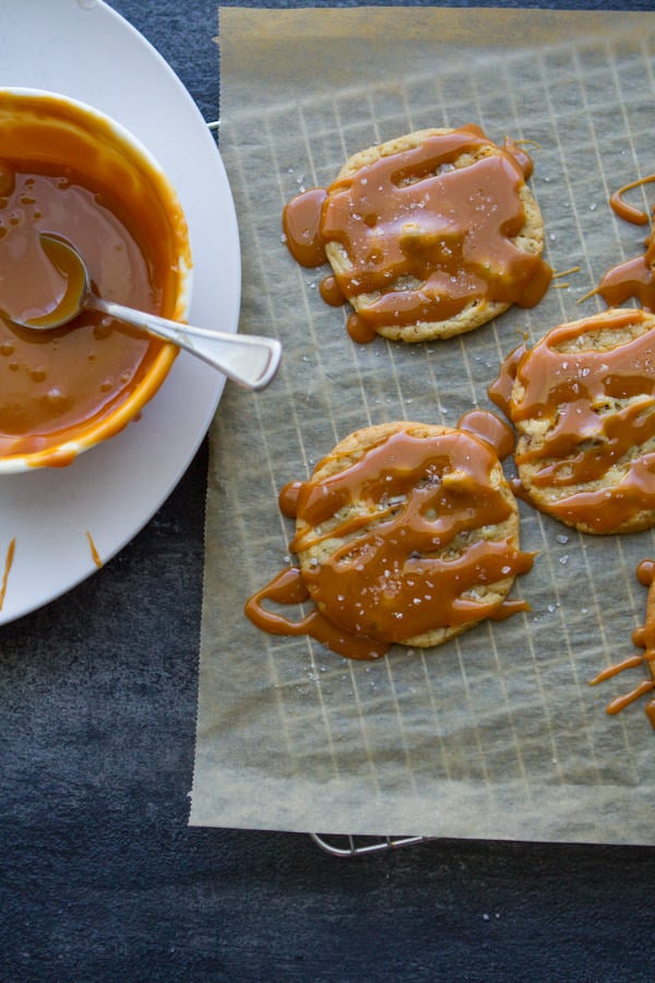 Salted Caramel Chocolate Chip Cookies on a cooling wrack next to a bowl of caramel ganache