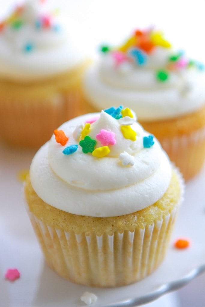 Sour Cream Vanilla Cupcakes with buttercream frosting and sprinkles on a cake platter