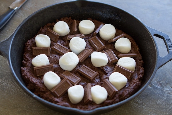 chocolate cookie dough in a skillet with chocolate bars and marshmallows