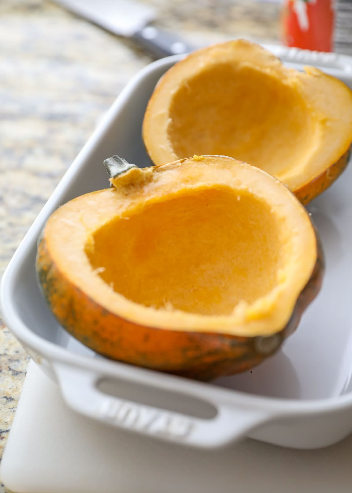 halved acorn squash cleaned out in white baking pan