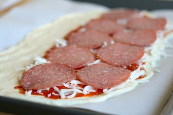 salami slices on top of cheese on top of sauce all over rolled out pizza dough