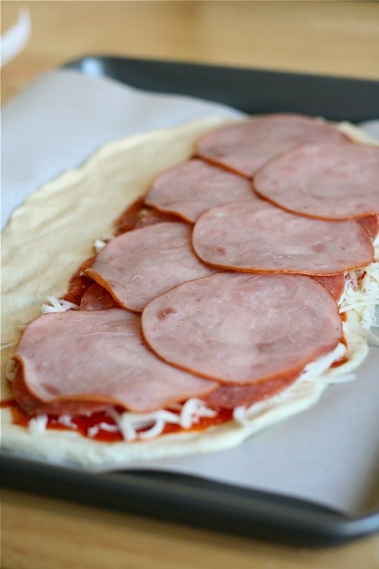 ham slices topping all the other toppings on rolled out stromboli dough
