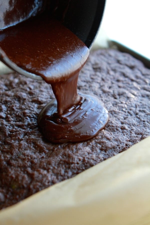 pouring chocolate glaze over zucchini brownies