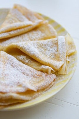 crepes on a plate with powdered sugar sprinkled on top.