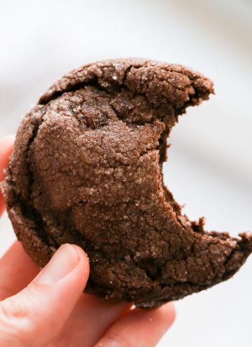 Chocolate fudge cake mix cookie with a bite taken out, held in one hand.