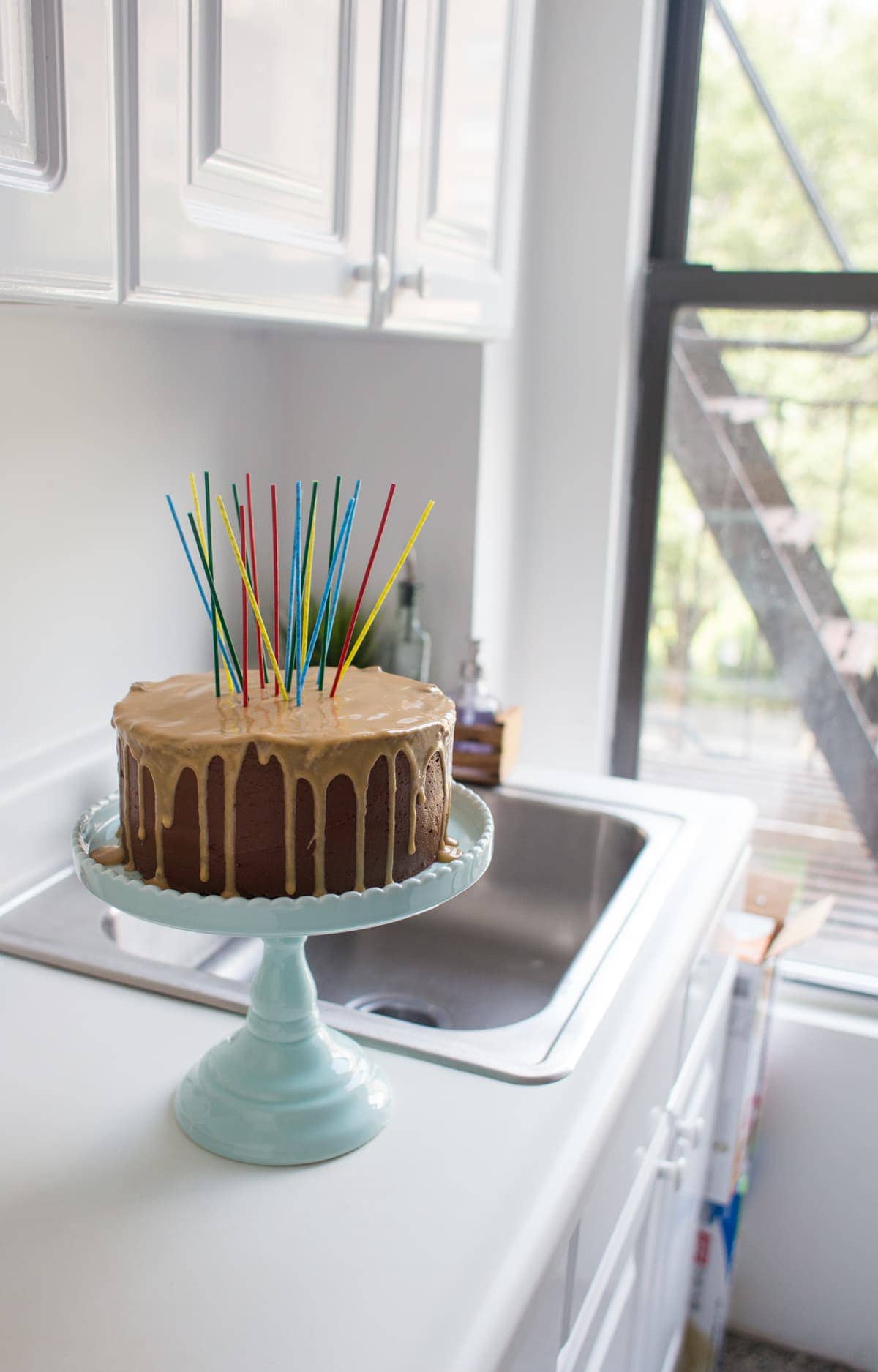 chocolate birthday cake with peanut butter glaze on a cake stand with candles sticking out of the top