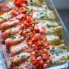enchiladas with half green and half red sauce on top of it. all topped with melted cheese, tomatoes and cilantro