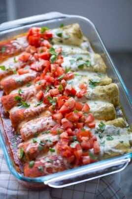 enchiladas with half green and half red sauce on top of it. all topped with melted cheese, tomatoes and cilantro