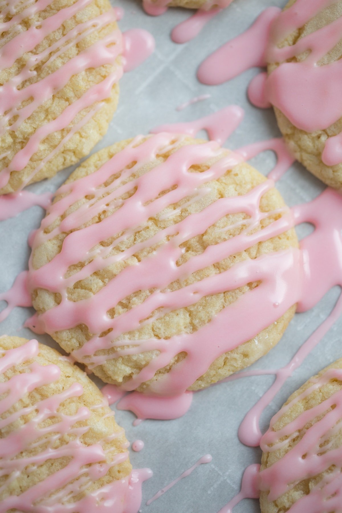 Sugar Cookies on parchment paper drizzled with pink icing