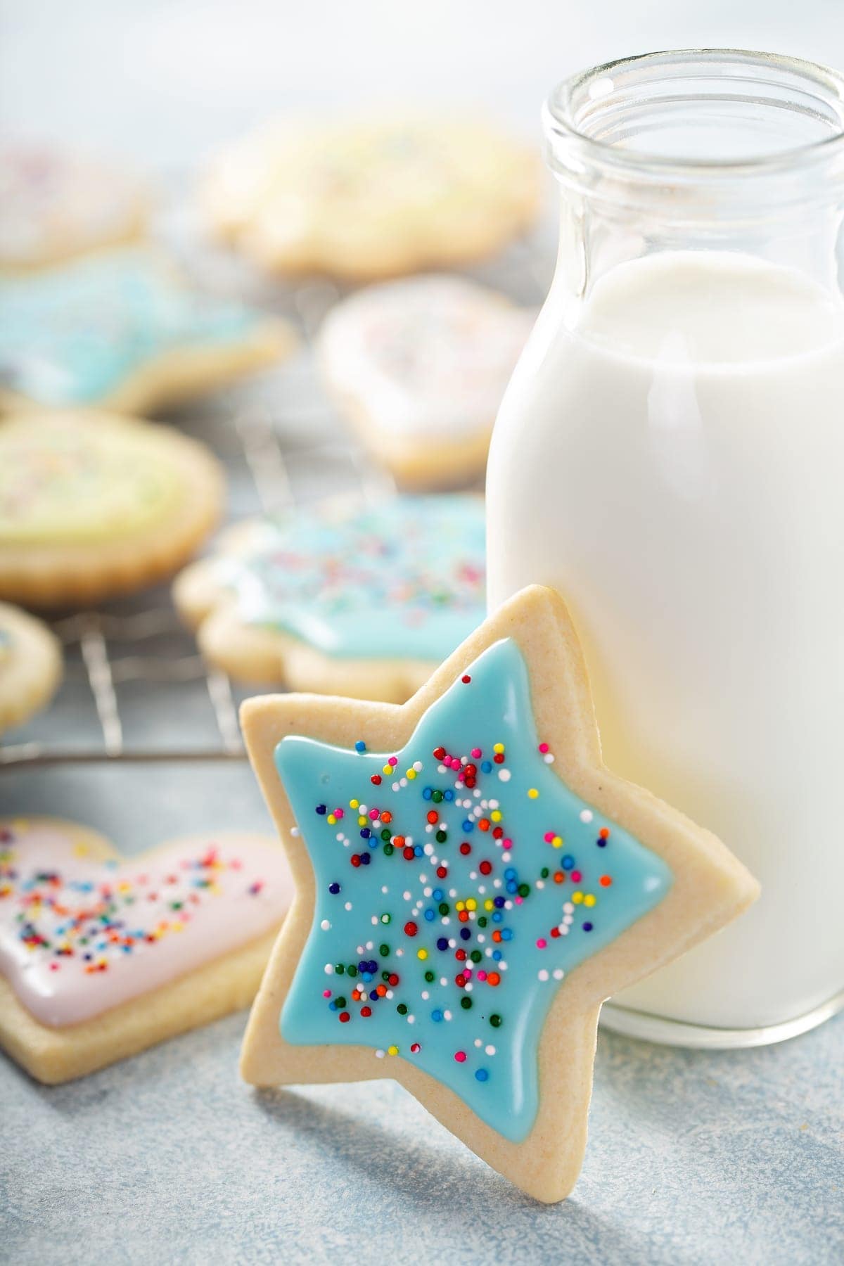 star shaped sugar cookie leaning on a glass of milk with other shaped sugar cookies in the background