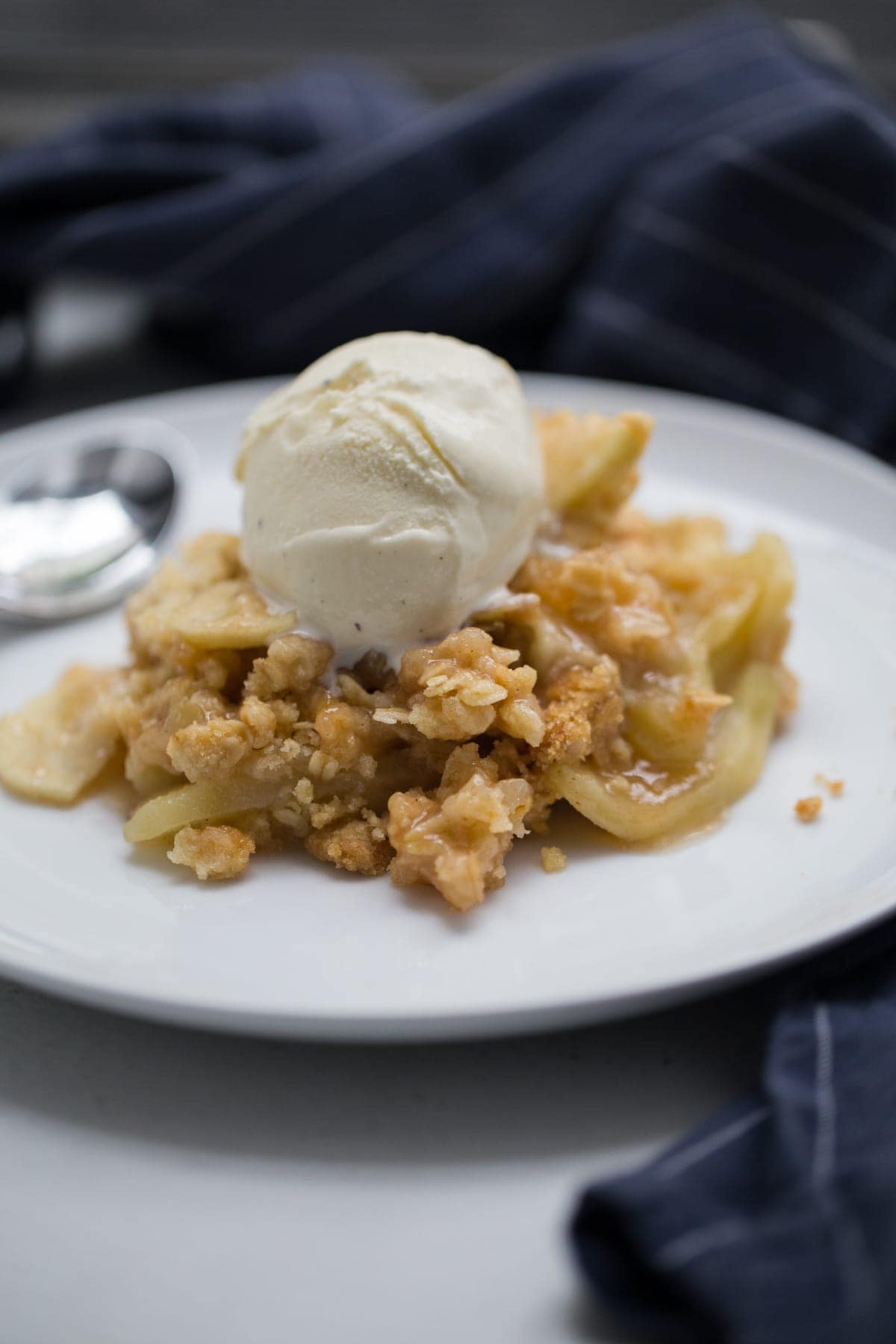 apple crisp topped with vanilla ice cream all on a white plate