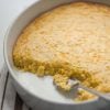 partial corn casserole in a round pan with a serving spoon