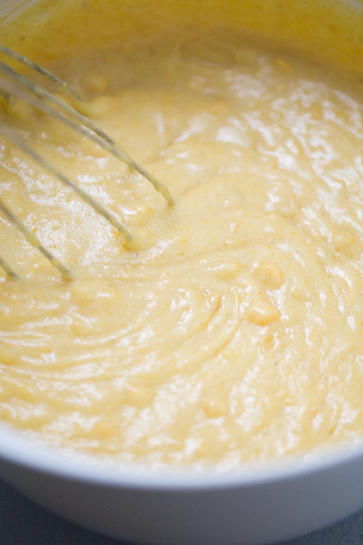 Cornbread batter in a white bowl being mixed with a whisk