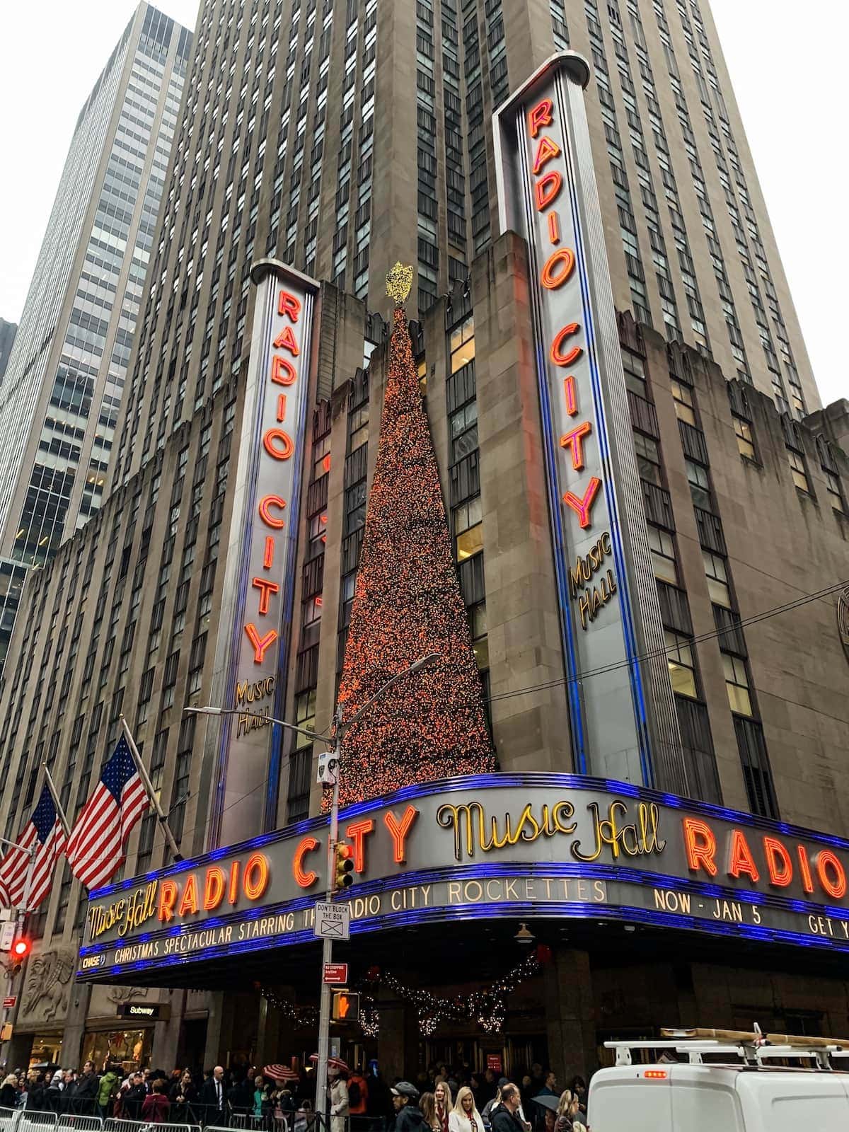 A group of people in a large city with Radio City Music Hall in the background
