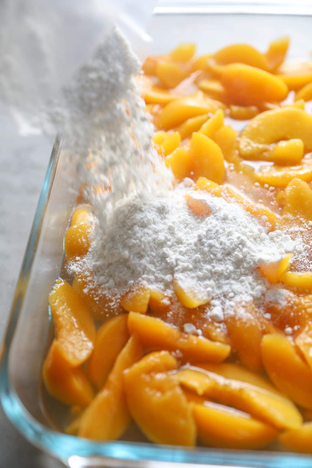 adding cake mix to canned peaches in baking dish