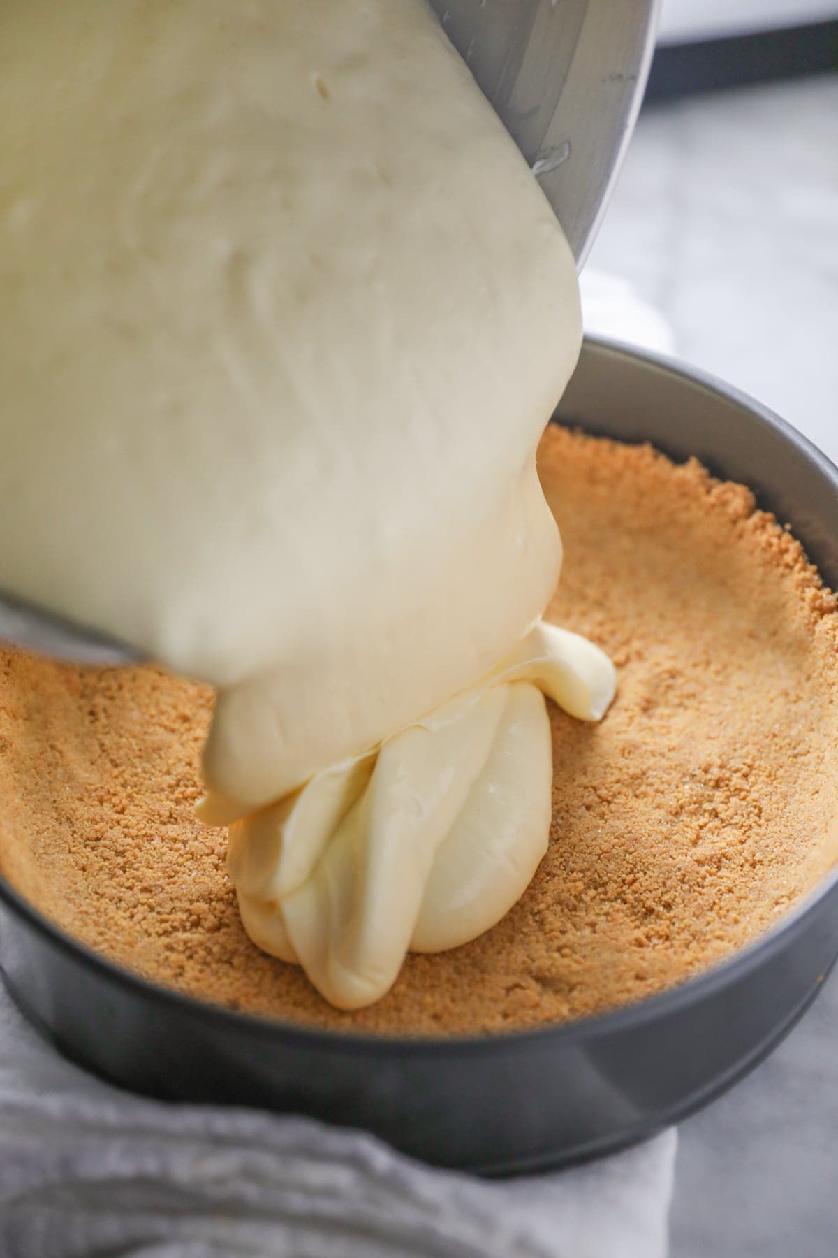 pouring cheesecake filling into graham cracker crust