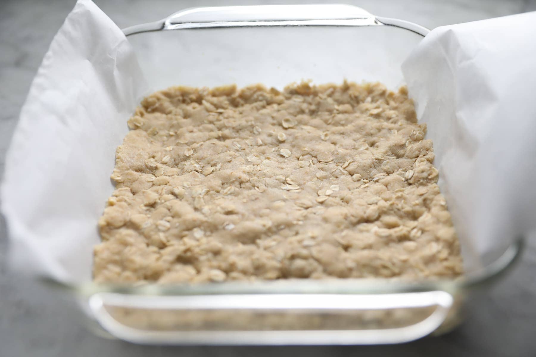 Oatmeal Cookie Dough pushed into a parchment paper lined square baking dish