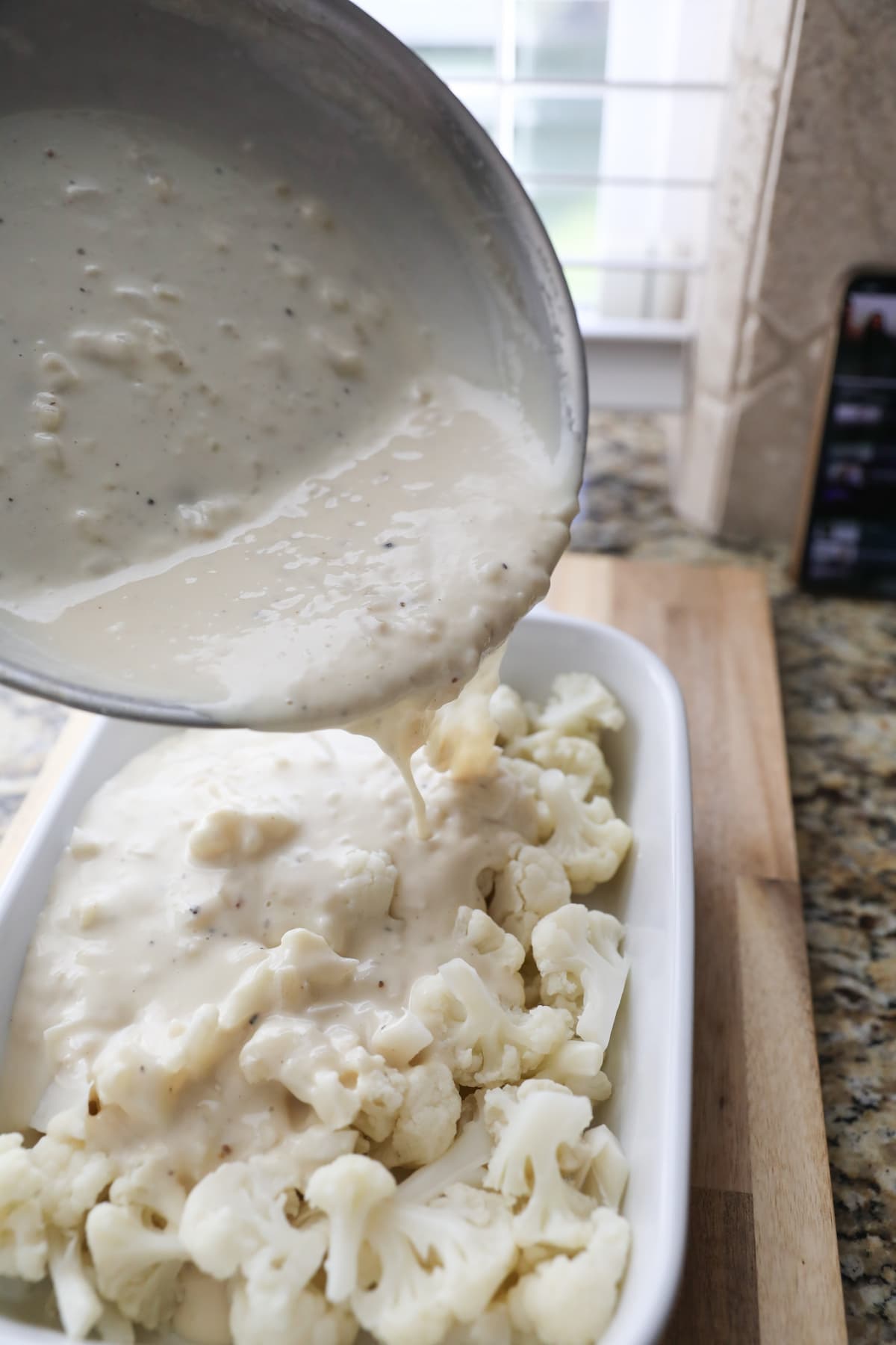 pouring white sauce over cauliflower